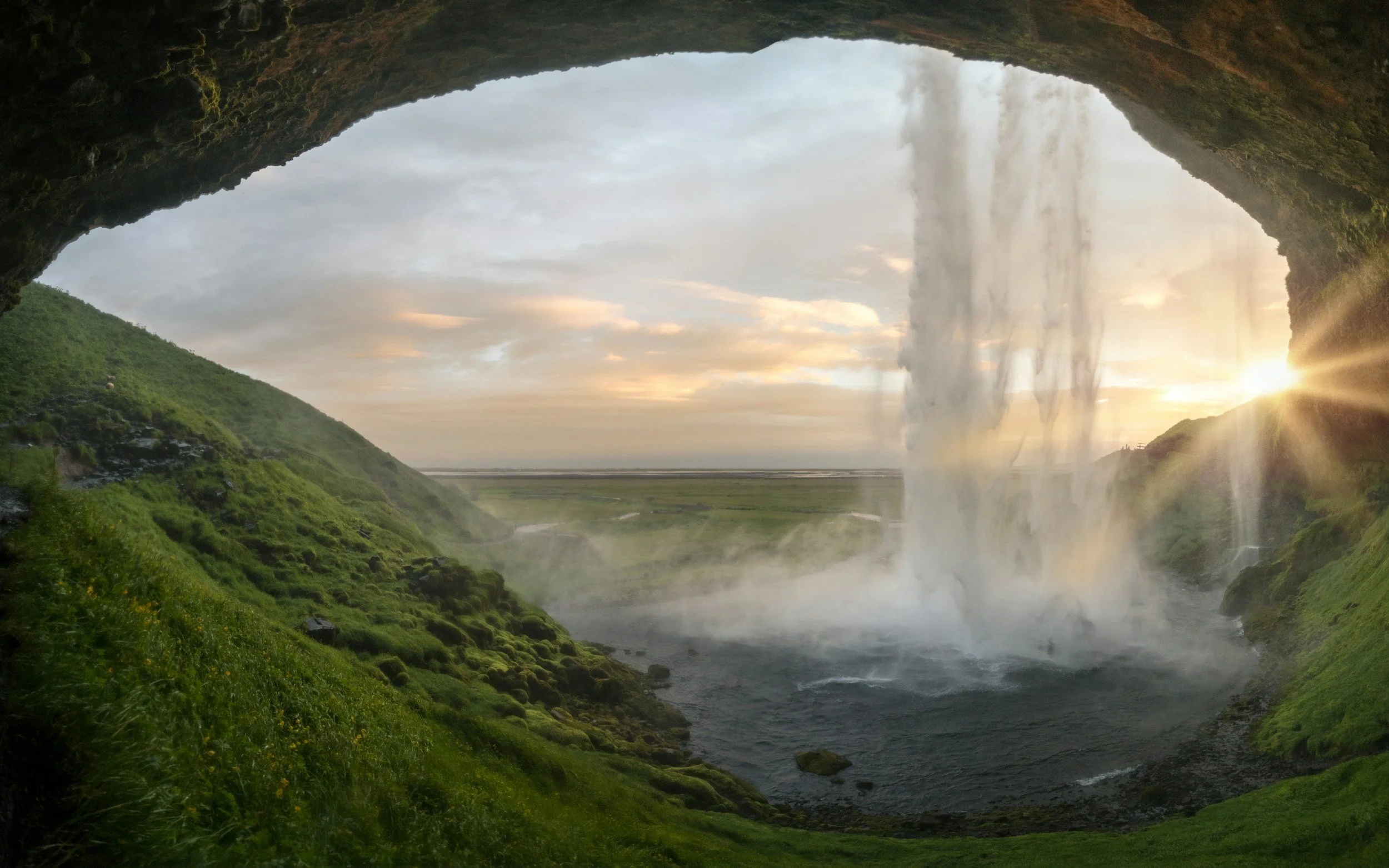 Golden sunlight breaking through a waterfall, seen from inside a dark grotto